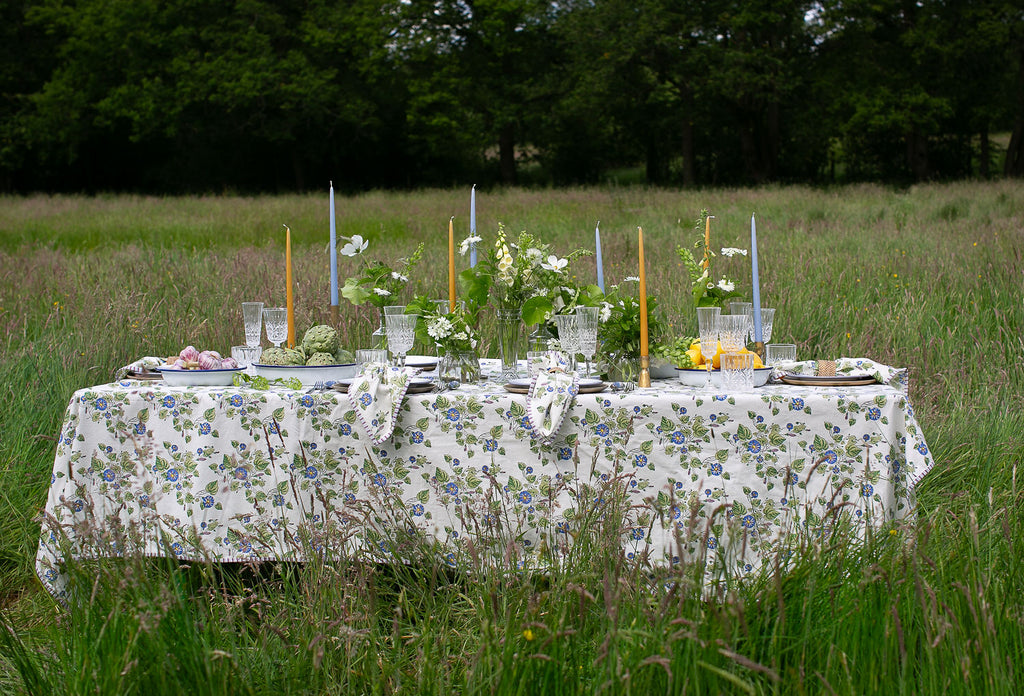 a  table  in a wild field set for lunch with a block printed tablecloth and napkins to match in a Morning Glory design 