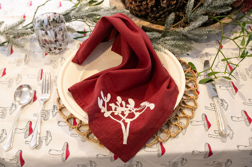 a claret coloured linen napkin with an embroidered mistletoe motif 