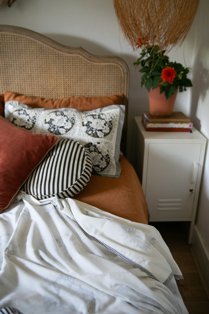 A dohar draped on a bed with a terracotta pot and a dahlia on a bedside cabinet