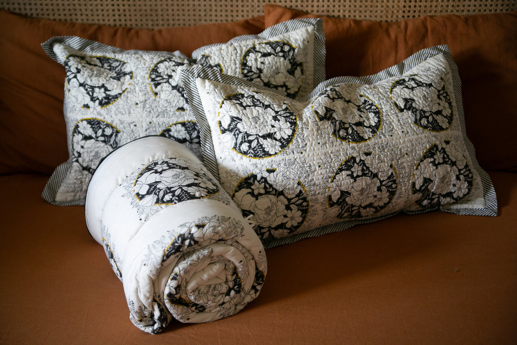 a block printed quilt and matching cushions on a rust coloured background 