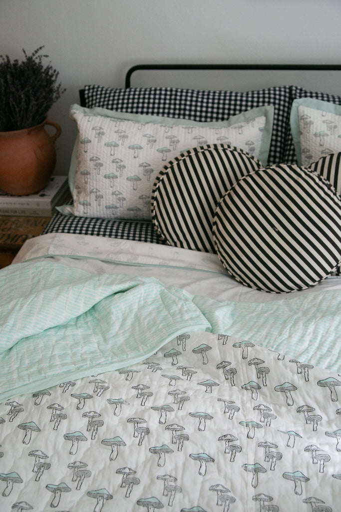 block printed mushroom design quilt on a bed with black and white round cushions