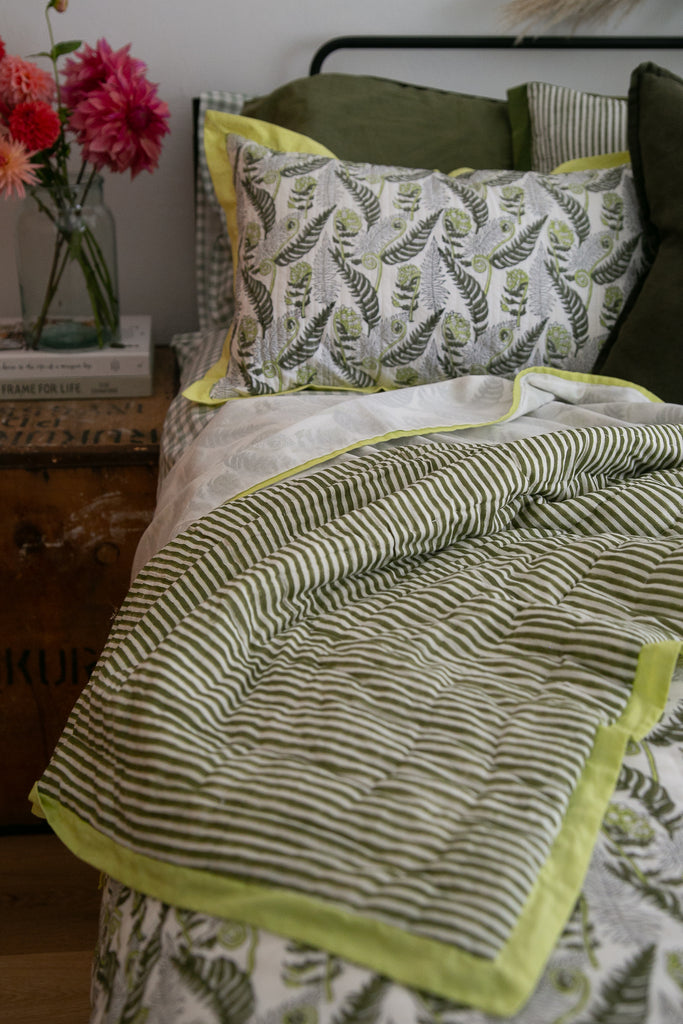 bed with a striped quilt and a glass vase of colourful dahlias 