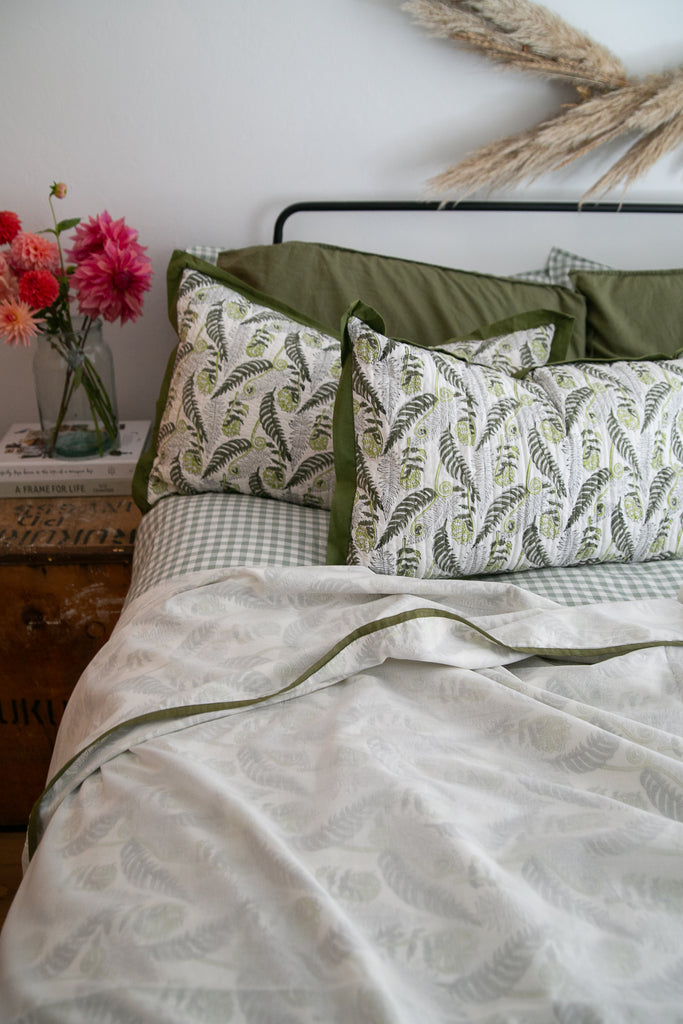 a bed made with a fern printed Dohar and a vase of colourful dahlias on a bedside cupboard 