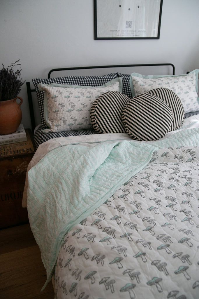 cosy looking bed with turquise mushroom bedding displayed  on gingham sheets 