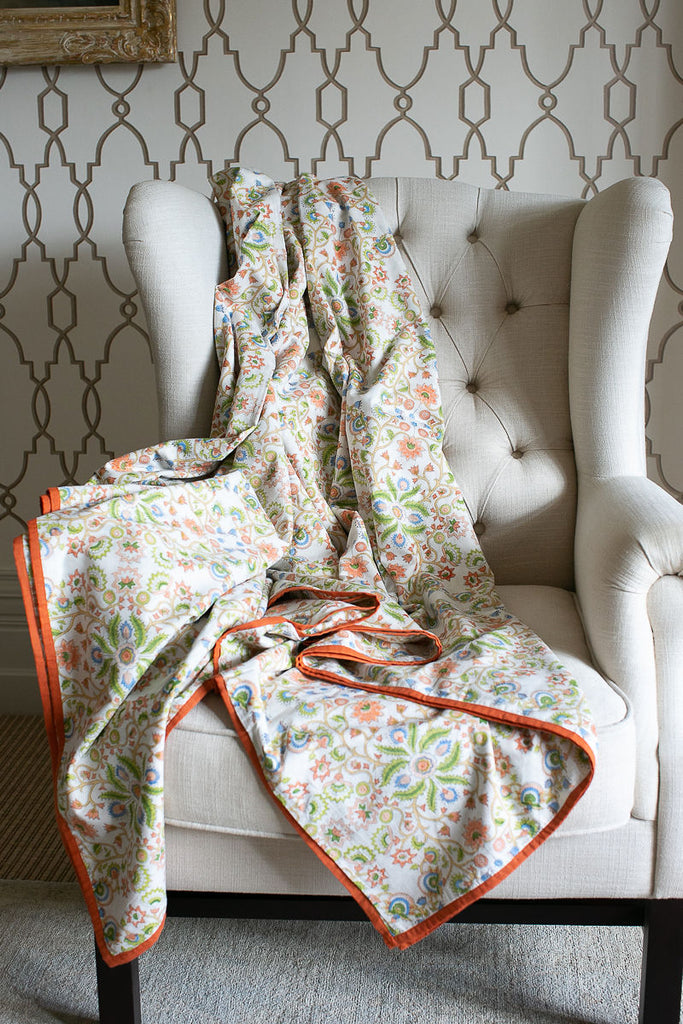 a colourful block-printed dohar with an orange border draped on a white chair