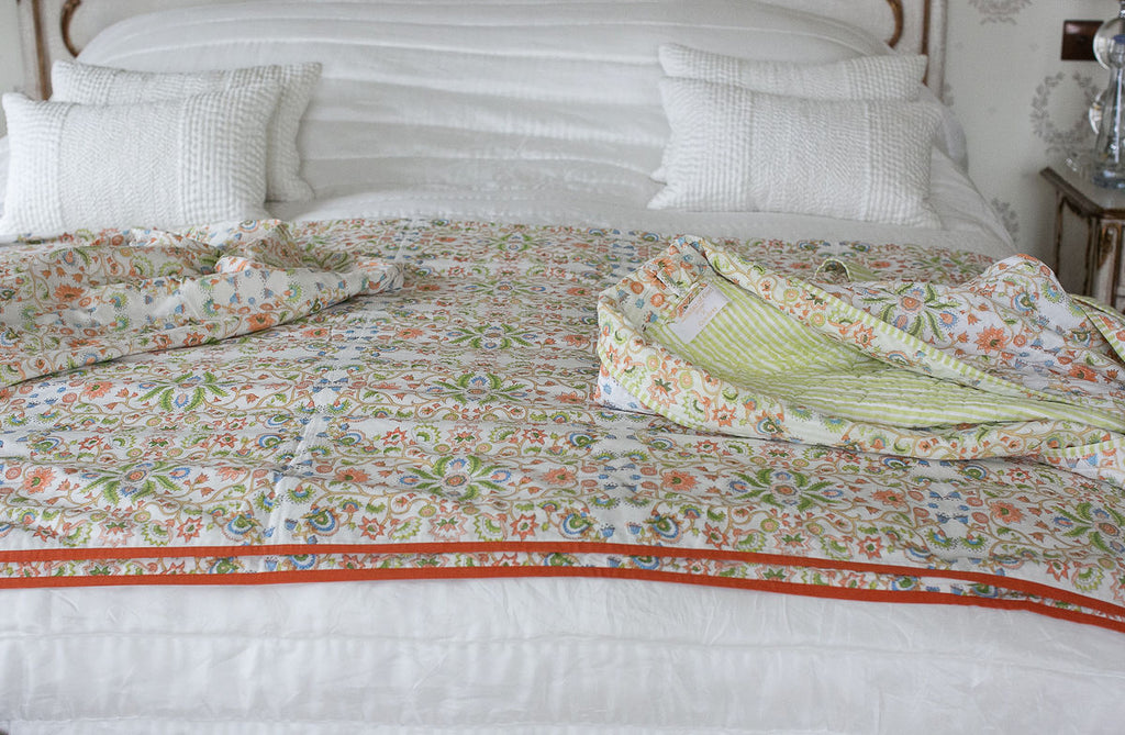 a bed made up with white bedlinen and a colourful block printed dohar with orange edging 