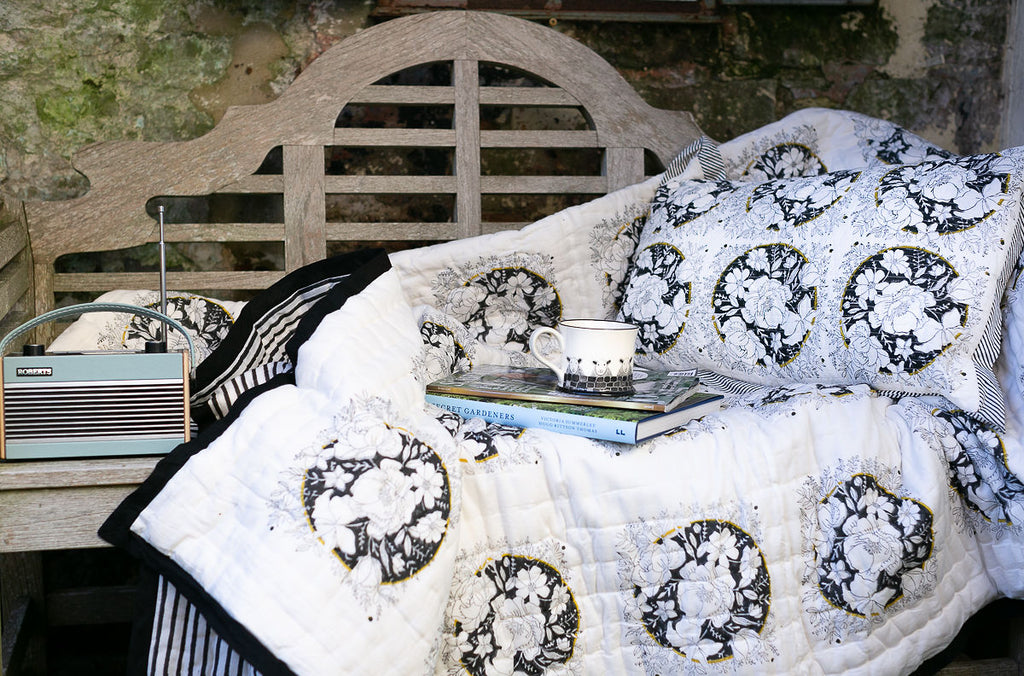 garden bench with a block printed cushion a cup of tea, a couple of books on a quilt and a radio 