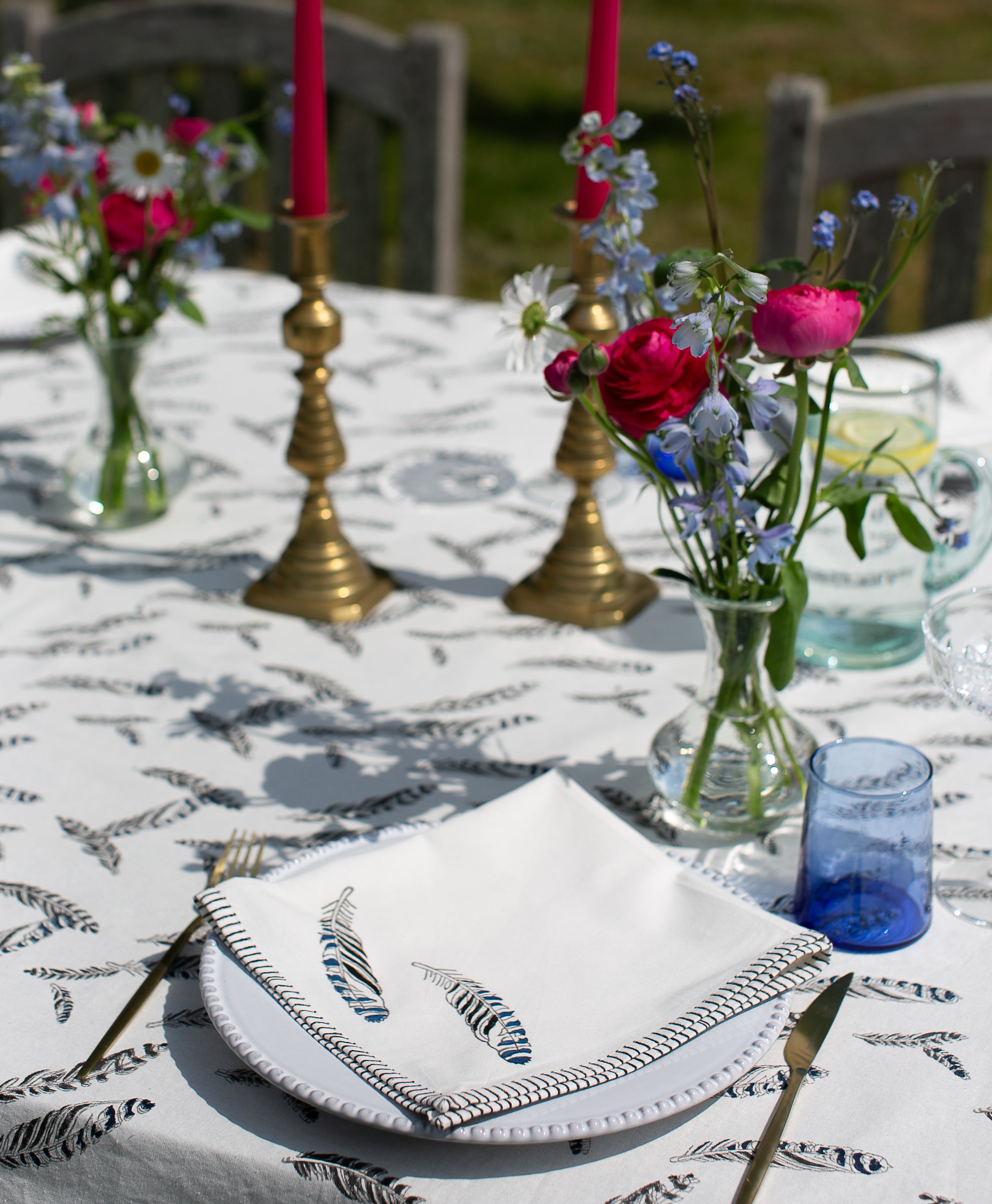close up of a feather block printed napkin on a table with a matching tablecloth and flowers 