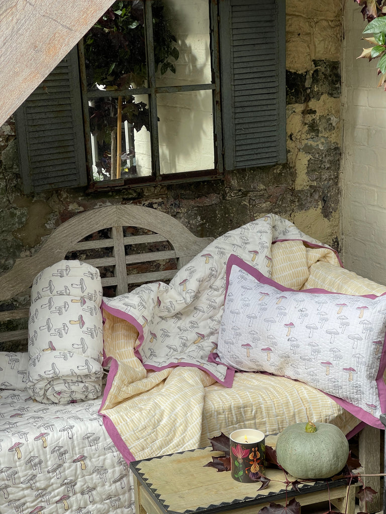 One block printed cushions and  two quilts in a wild mushroom design on a garden bench 