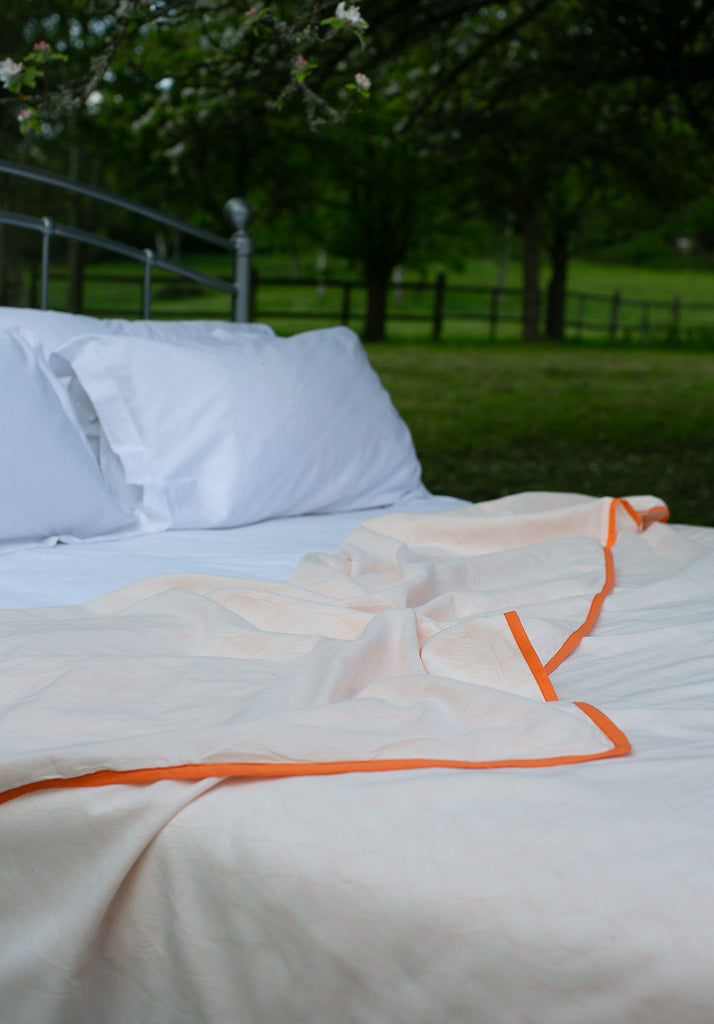 detail of a bed in the garden made up with a tangerine block printed dohar 