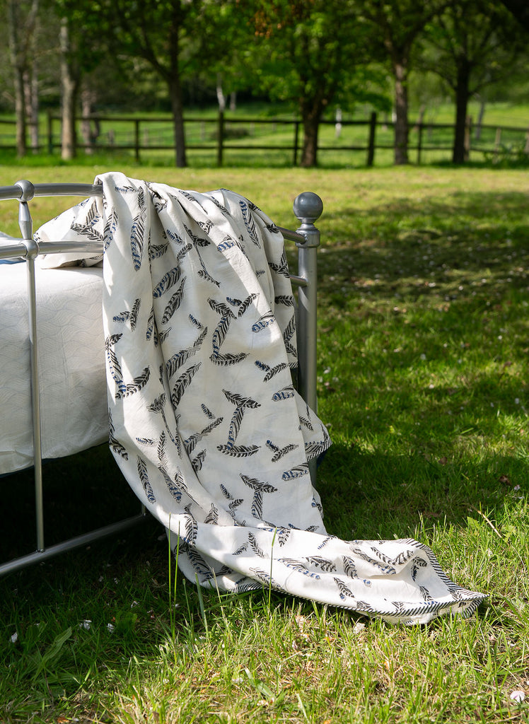 a dohar block printed with a jay feather pattern draped on a bed outside