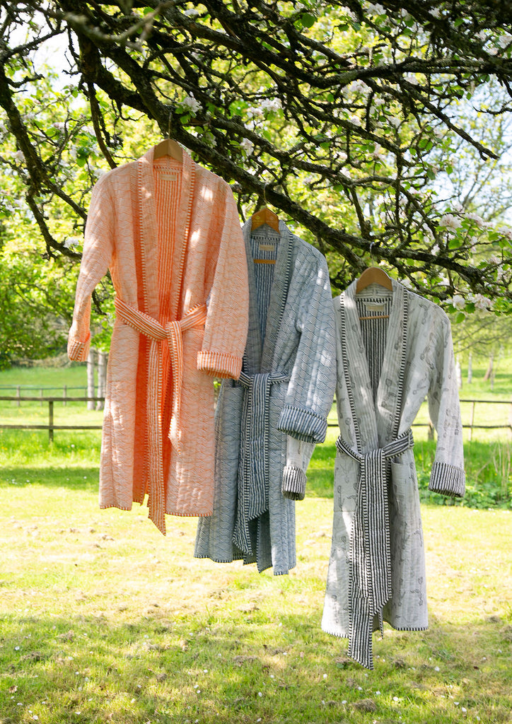 three blockprinted dressing gowns hanging from a branch of an apple tree 