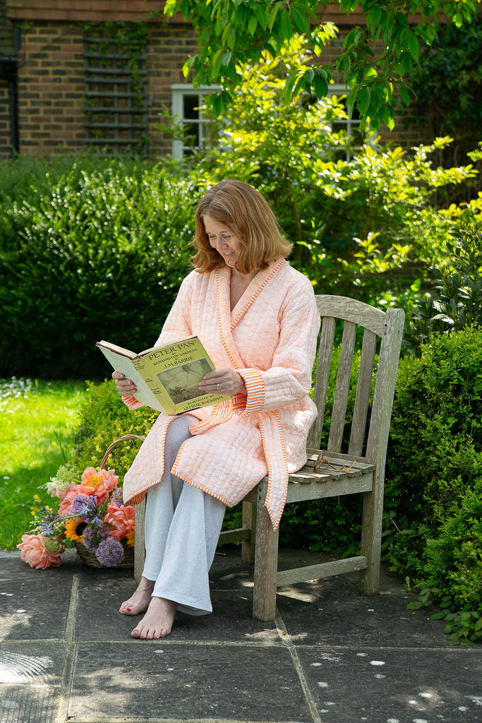 lady reading a book sitting on a chair wearing an orange quilted dressing gown 