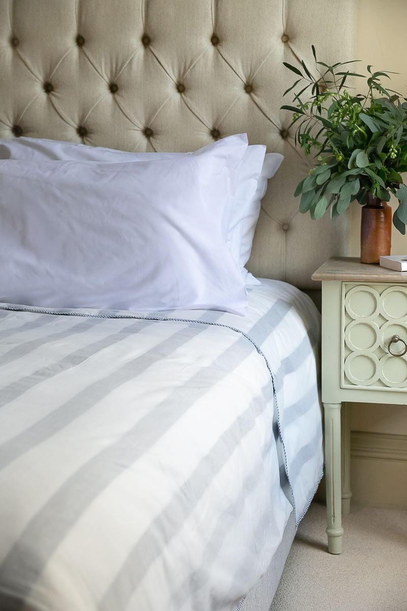 Neatly made bed with striped bedding and white pillows, next to a nightstand with a plant.
