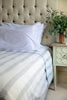 Neatly made bed with striped bedding and white pillows, next to a nightstand with a plant.