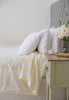 Bed with white bedding and yellow striped Dohar blanket next to a nightstand with flowers.