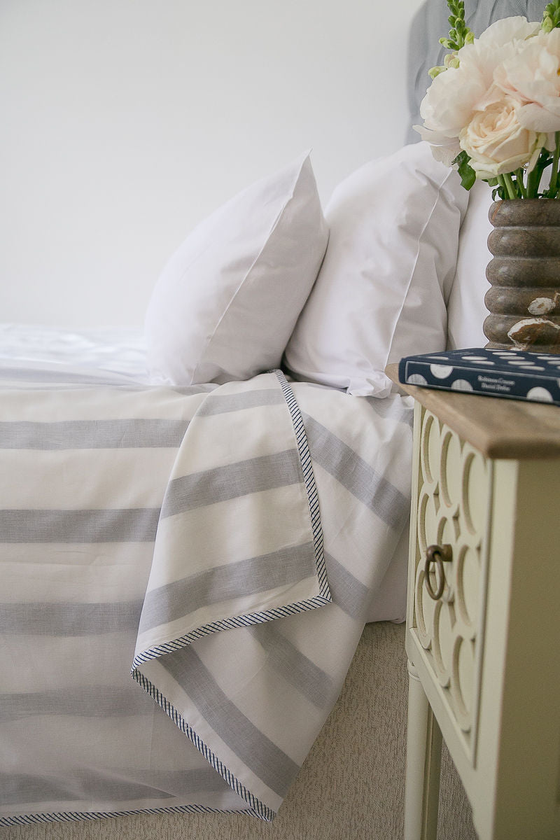 Blue and white striped Dohar blanket on a bed with a nightstand and flowers.