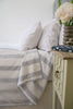 Blue and white striped Dohar blanket on a bed with a nightstand and flowers.