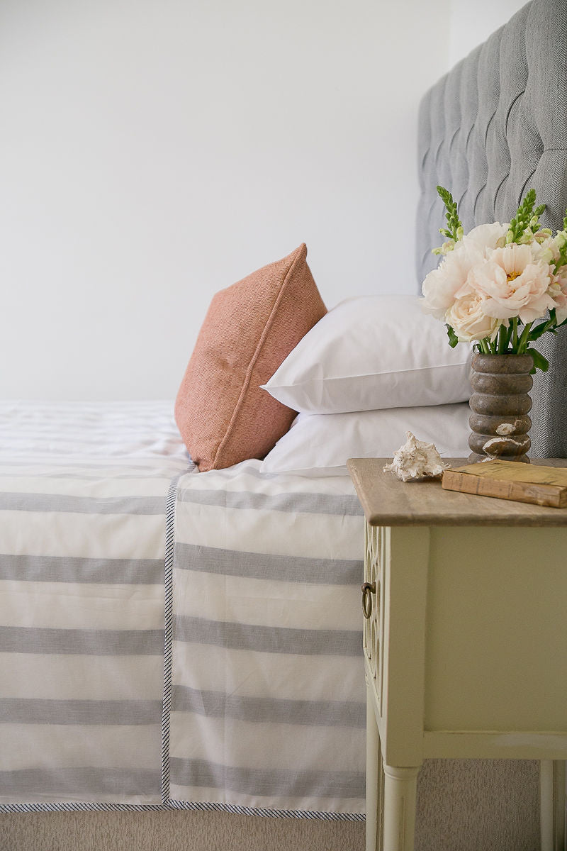 Bed with striped bedding, pillows, and a vase of flowers on a nightstand.