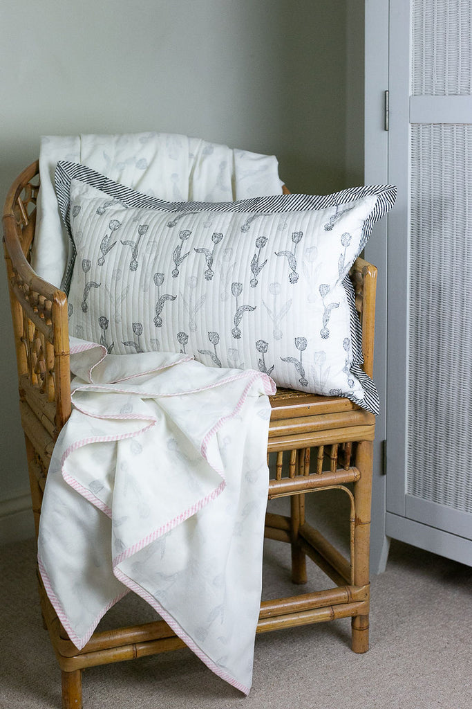 a tulip block printed dohar with pink edgings draped on a cane chair with a matching cushion 