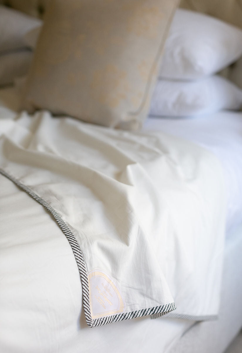 Close-up of a white Dohar Blanket with decorative striped edging on a bed.