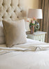Neatly made bed with a cotton Dohar and a tufted headboard, lamp, and vase on a nightstand.