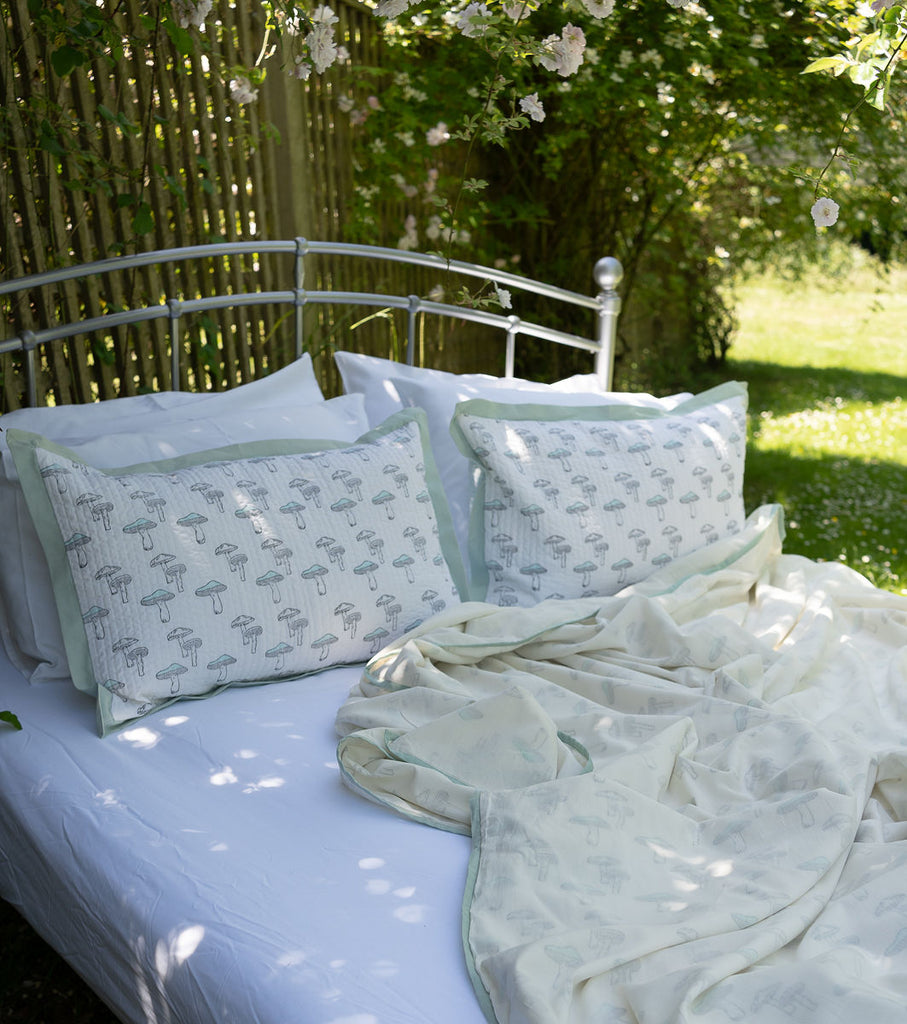 2 cushions and a matching dohar on a bed outside in a turquoise mushroom print 