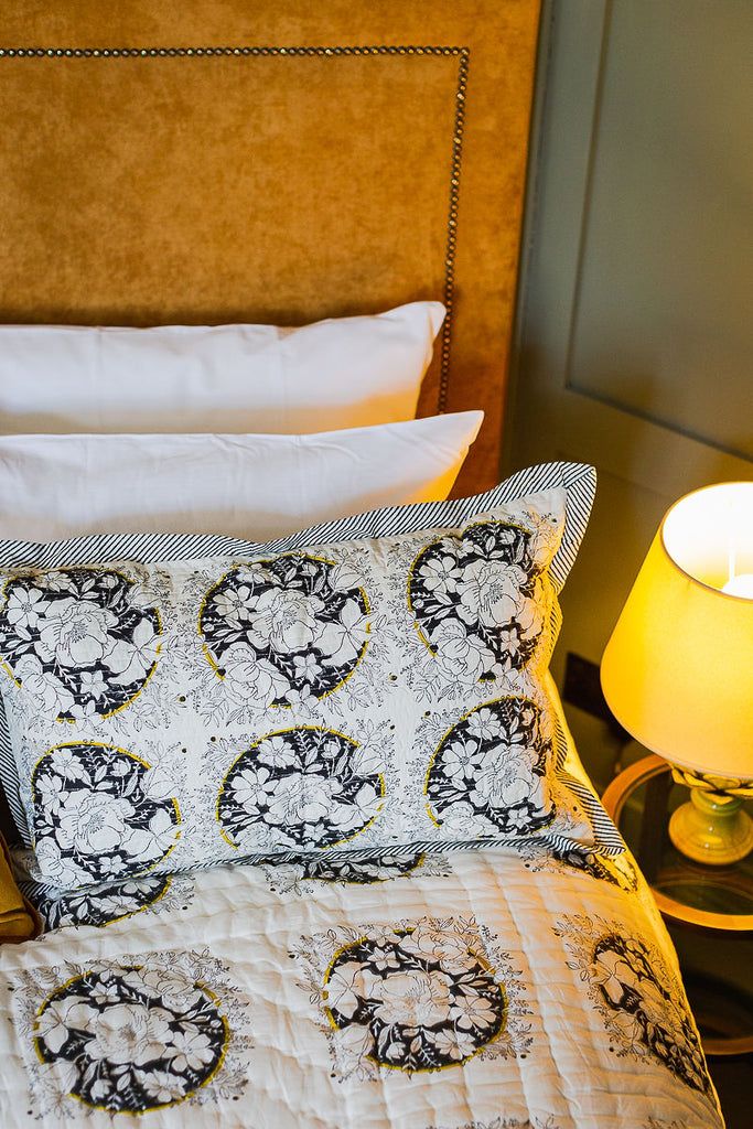 back and white block printed pillow on a bed with a lamp 