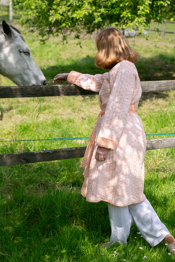 lady feeding a horse over a fence wearing a block printed orange quilted robe 