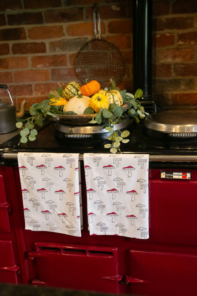 two block printed tea towels hanging from a burgundy Aga